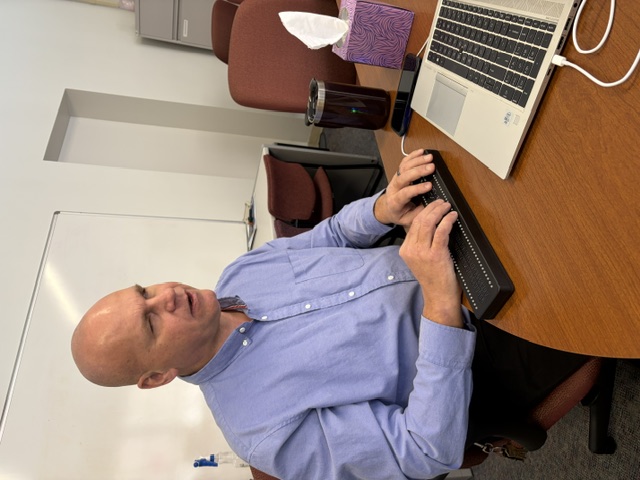 A person using a single-line Braille display while working at a desk